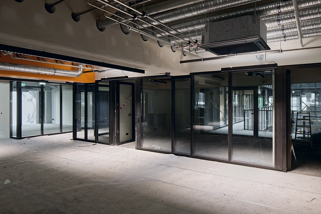 Architekturfoto einer Büroetage kurz vor Fertigstellung. Weitläufiger Flur mit Glaseinbauten als Büros und offener Deckenkonstruktion.