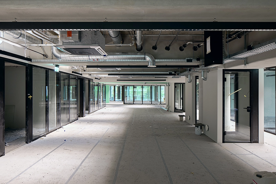 Architekturfoto einer Fabriketage, die als Bürofläche genutzt wird. Eine Baustelle kurz vor Fertigstellung. Ein langer Gang mit offener Deckenkonstruktion.