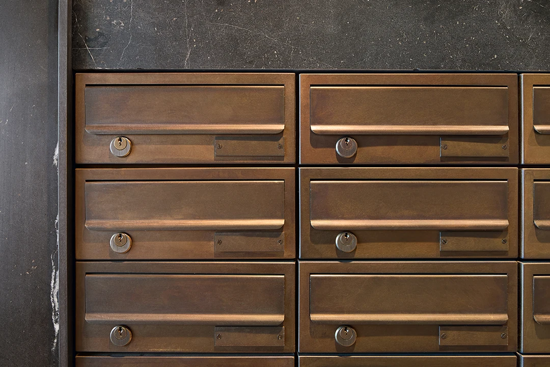 Detailaufnahme von Briefkästen aus Bronze vor schwarzem Naturstein, warm ausgeleuchtet