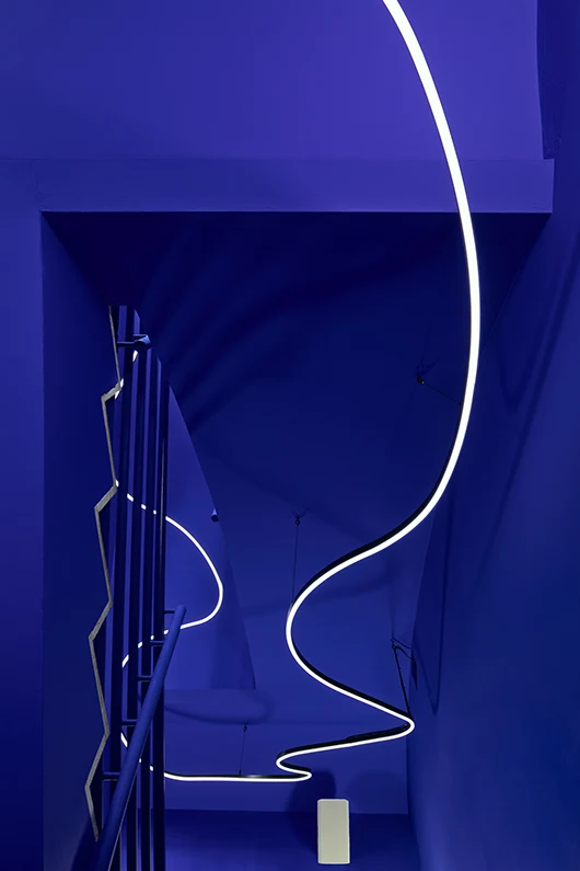 Architekturfotografie des kräftig blauen Treppenhauses im Exilmuseum Berlin. Blaue Wände, blaue Geländer und eine geschwungene Linie als Beleuchtung. Anspruchsvolle Architekturfotografie.